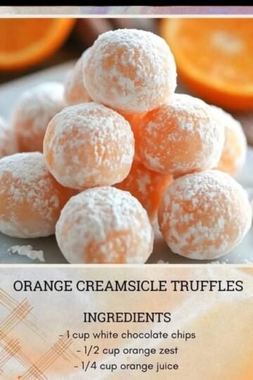 A stack of soft orange creamsicle truffles coated in powdered sugar, with a delicate citrus-orange center and fresh orange slices blurred in the background.
