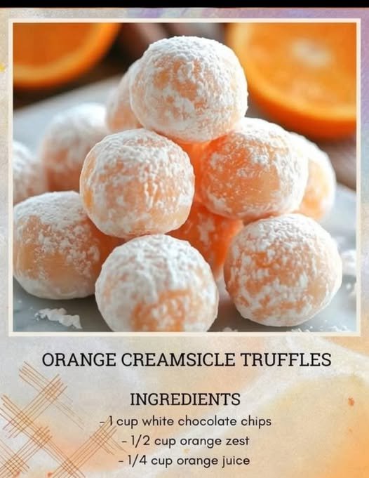 A stack of soft orange creamsicle truffles coated in powdered sugar, with a delicate citrus-orange center and fresh orange slices blurred in the background.