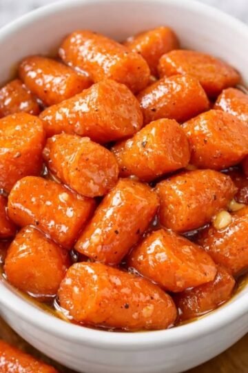 A bowl of tender baby carrots coated in a glossy, buttery-sweet glaze, seasoned with black pepper and caramelized until beautifully shiny.
