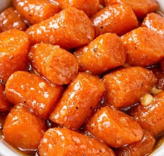 A bowl of tender baby carrots coated in a glossy, buttery-sweet glaze, seasoned with black pepper and caramelized until beautifully shiny.