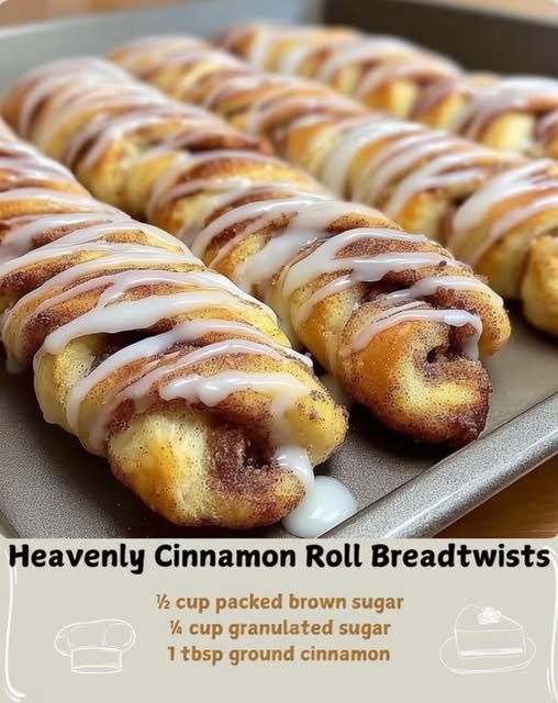 Golden-brown cinnamon roll bread twists arranged on a baking sheet, filled with cinnamon-sugar swirls and finished with a generous drizzle of white vanilla glaze.