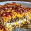 A close-up slice of bacon cheeseburger sheet pan lasagna layered with seasoned ground beef, creamy ricotta, melted cheddar cheese, and topped with crispy chopped bacon and fresh herbs.