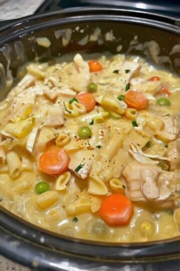 Creamy chicken pot pie noodle skillet filled with tender chicken, egg noodles, bright carrots and green peas in a rich, savory cream sauce, garnished with fresh herbs and black pepper.