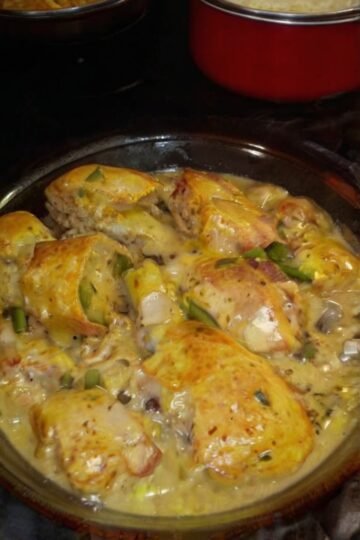 Golden-browned chicken legs smothered in a rich creamy mushroom sauce with sliced mushrooms, garlic, and herbs, served hot in a glass baking dish.