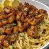 Juicy garlic-butter shrimp served over creamy pasta, glazed with a rich golden sauce, garnished with fresh parsley and lemon wedges.