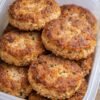 A container filled with crispy golden-brown salmon patties, featuring a savory flaky salmon interior, lightly browned crust, and small flecks of herbs throughout.