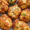Golden-brown cheesy chicken fritters with crisp, irregular edges and melted mozzarella inside, garnished with fresh dill and served on parchment paper.