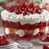 A layered cherry trifle in a clear glass dish, featuring juicy red cherries, fluffy whipped cream, and golden cake pieces, topped with whole cherries and cream.