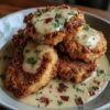 Golden-brown country-fried pork chops topped with crispy bacon and creamy peppered gravy, garnished with fresh parsley and served warm on a wooden board.