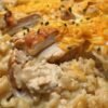 A creamy chicken and rice casserole topped with melted cheddar cheese, featuring tender pieces of chicken, fluffy rice, and a golden cheesy crust garnished with fresh chives.
