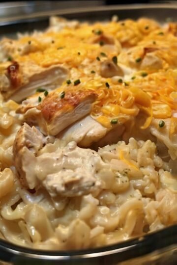 A creamy chicken and rice casserole topped with melted cheddar cheese, featuring tender pieces of chicken, fluffy rice, and a golden cheesy crust garnished with fresh chives.