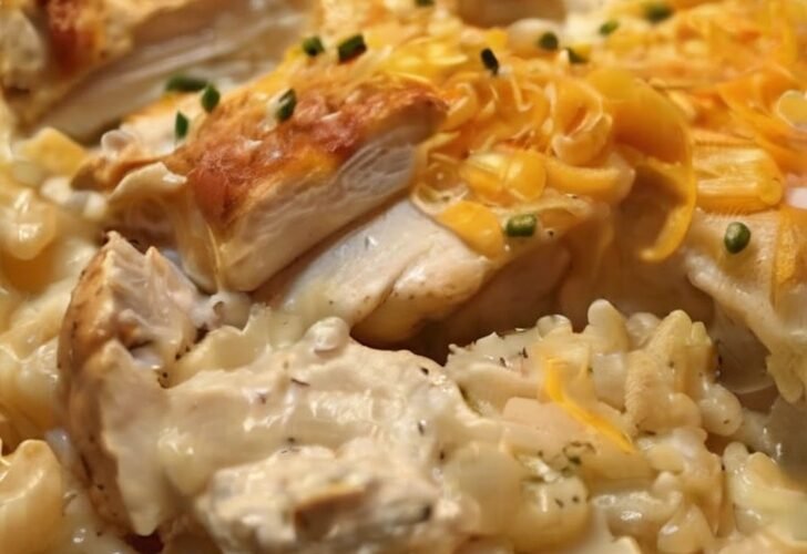 A creamy chicken and rice casserole topped with melted cheddar cheese, featuring tender pieces of chicken, fluffy rice, and a golden cheesy crust garnished with fresh chives.