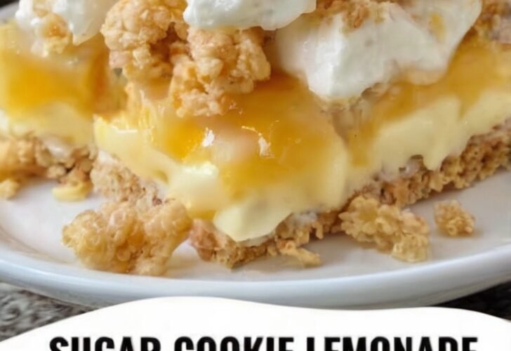 A slice of sugar cookie lemonade crumble topped with creamy lemon filling, whipped cream, and golden buttery cookie crumbs, with a bright lemon in the background.