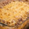 A bubbling ground beef and corn casserole baked in a glass dish, topped with a golden layer of melted cheddar cheese and lightly browned around the edges.