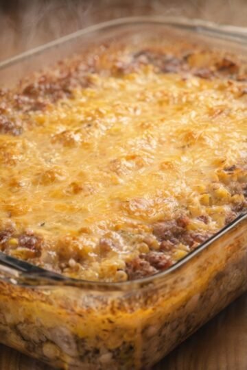 A bubbling ground beef and corn casserole baked in a glass dish, topped with a golden layer of melted cheddar cheese and lightly browned around the edges.