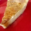 A slice of creamy old-fashioned custard pie with a smooth, rich filling and a golden caramelized top, served on a bright red plate.