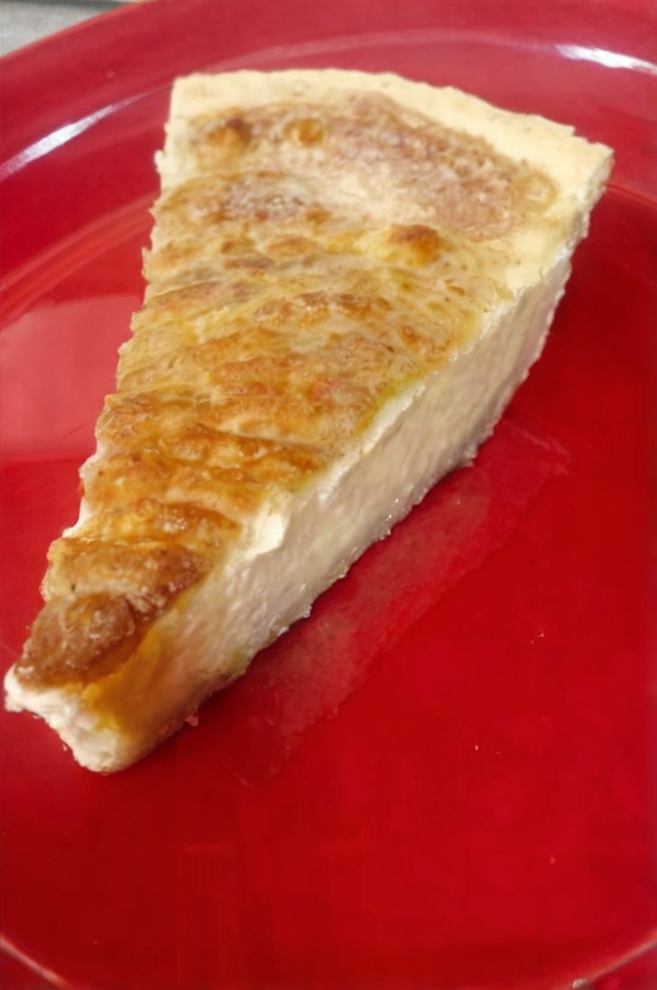 A slice of creamy old-fashioned custard pie with a smooth, rich filling and a golden caramelized top, served on a bright red plate.