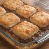 Golden-brown flaky biscuits baked over a rich, savory ground beef filling in a glass casserole dish, creating a hearty and comforting one-pan meal.