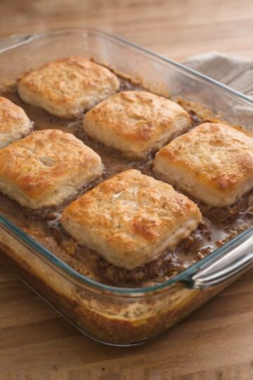 Golden-brown flaky biscuits baked over a rich, savory ground beef filling in a glass casserole dish, creating a hearty and comforting one-pan meal.