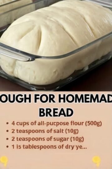 A large, smooth mound of homemade bread dough rising in a clear glass baking dish, with the soft, elastic surface visibly puffed and ready to bake.