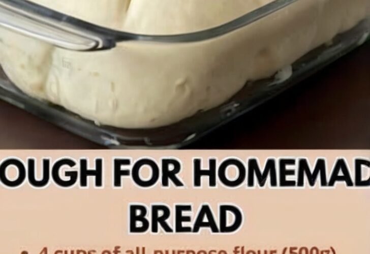 A large, smooth mound of homemade bread dough rising in a clear glass baking dish, with the soft, elastic surface visibly puffed and ready to bake.