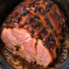 Four golden-brown pork chops topped with melting butter and herbs, each wrapped in crinkled aluminum foil inside a white slow cooker, with savory juices pooling around the tender, juicy meat.