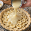 A homemade banana cream pie in a flaky pastry crust, layered generously with fresh banana slices and a thick, silky sweetened condensed milk filling being poured over the top. cooks.com