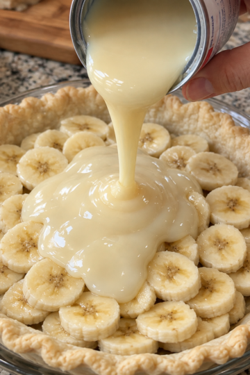 A homemade banana cream pie in a flaky pastry crust, layered generously with fresh banana slices and a thick, silky sweetened condensed milk filling being poured over the top. cooks.com
