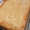 A golden, flaky pastry-topped casserole baked in a rectangular glass dish, with a beautifully crisp, buttery crust and lightly browned edges. simplyhappenings.com