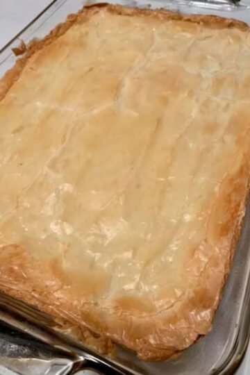 A golden, flaky pastry-topped casserole baked in a rectangular glass dish, with a beautifully crisp, buttery crust and lightly browned edges. simplyhappenings.com
