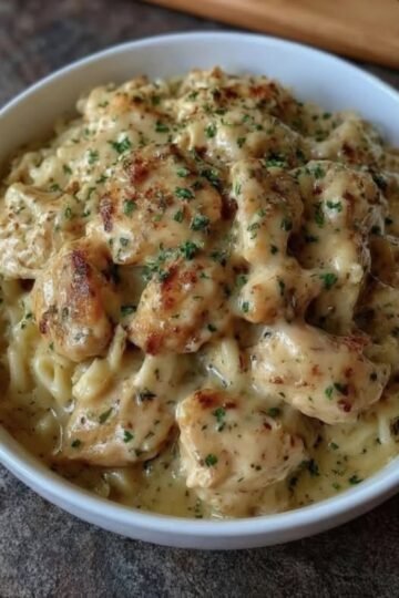A comforting bowl of creamy chicken pasta featuring tender, golden-browned chicken pieces coated in a rich garlic-Parmesan sauce, tossed with pasta and finished with fresh chopped parsley