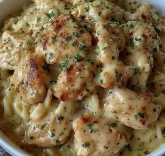 A comforting bowl of creamy chicken pasta featuring tender, golden-browned chicken pieces coated in a rich garlic-Parmesan sauce, tossed with pasta and finished with fresh chopped parsley