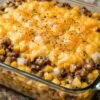 A hearty ground beef and potato casserole layered with tender potatoes, savory seasoned beef, sweet corn, and vegetables, all covered in a generous layer of melted, golden cheddar cheese and cracked black pepper.