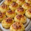 Golden-brown cheesy potato balls with crisp, caramelized tops and a soft, fluffy potato center, beautifully arranged on a decorative serving platter.