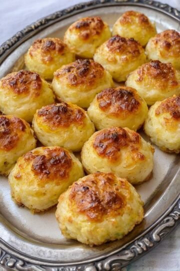 Golden-brown cheesy potato balls with crisp, caramelized tops and a soft, fluffy potato center, beautifully arranged on a decorative serving platter.