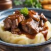 Tender beef tips smothered in rich brown gravy and served over creamy mashed potatoes, garnished with fresh parsley for a comforting homestyle meal.