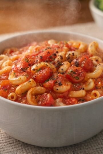 A comforting bowl of elbow macaroni tossed in a rich, chunky tomato sauce, topped with cracked black pepper and served piping hot for a simple, hearty homemade meal.